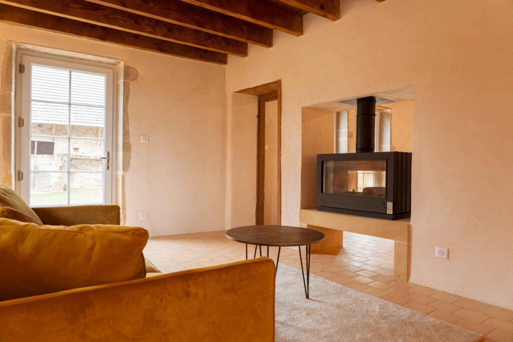 Photographie de la rénovation d'une maison dans le Beaujolais. On y voit un salon avec un insert et de l'enduit à la chaux crème sur les murs.